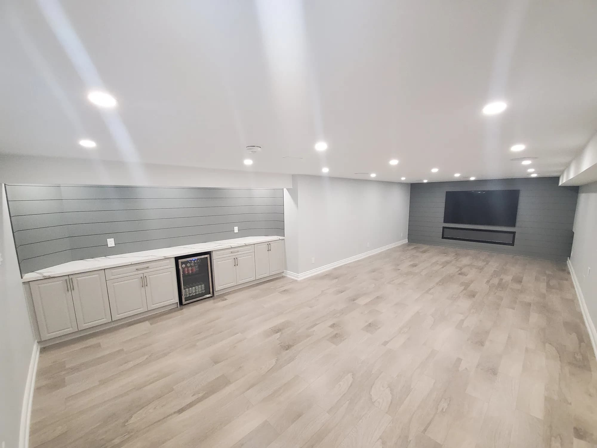 Modern basement with grey shiplap feature wall, bar cabinets, and entertainment center