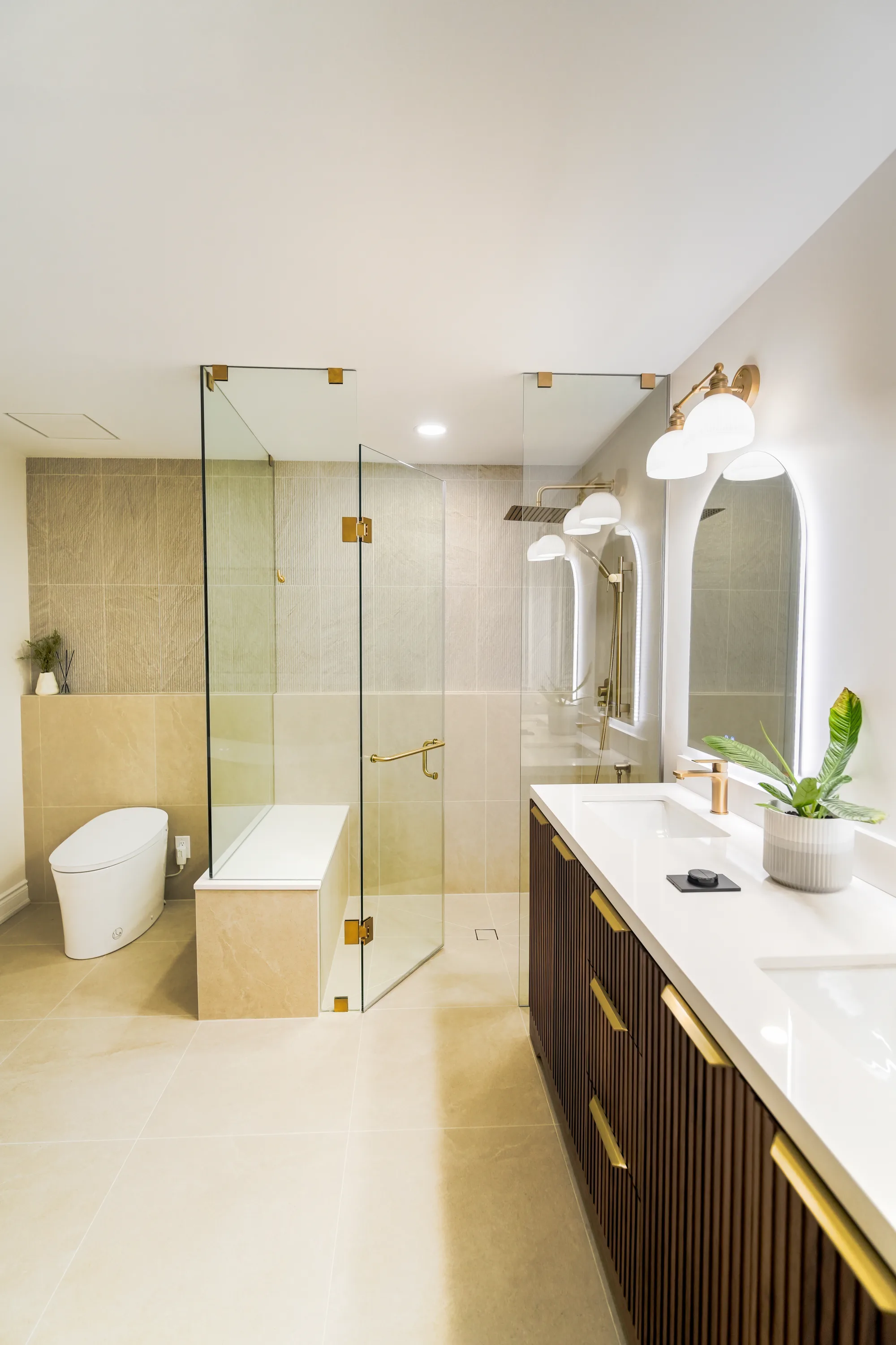 Luxury bathroom with walnut double vanity, arched mirrors, walk-in shower, and gold fixtures