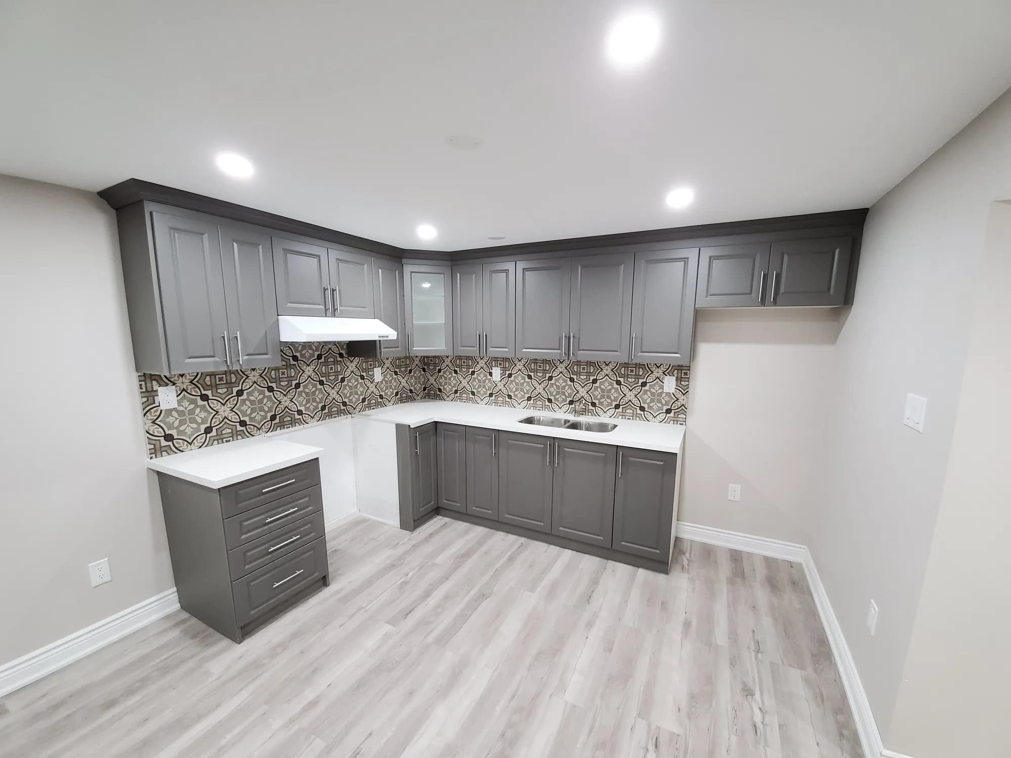 Basement kitchen with grey shaker cabinets, decorative mosaic tile backsplash, and quartz countertop