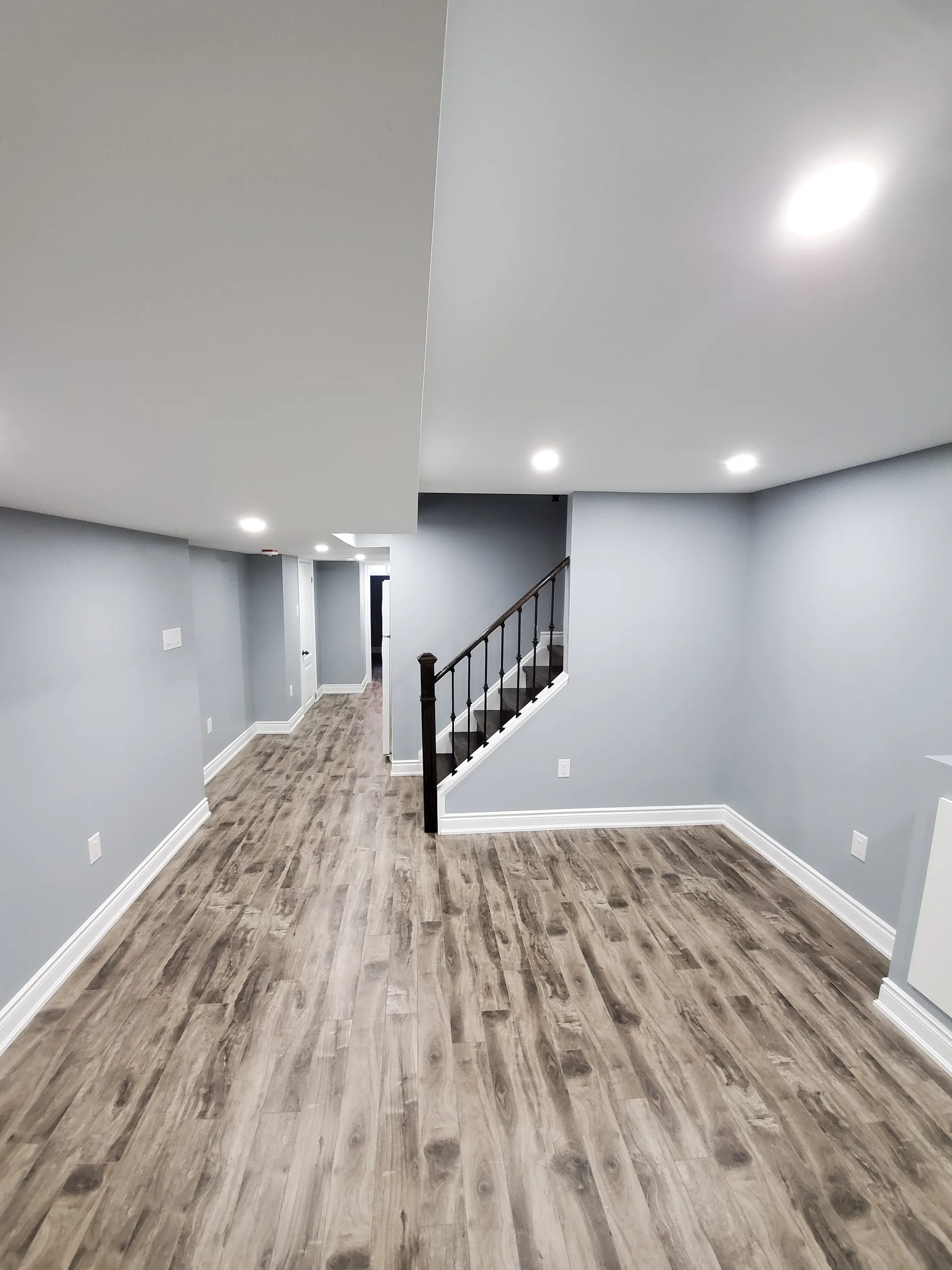 Finished basement living area with blue-grey walls and staircase with black iron railing