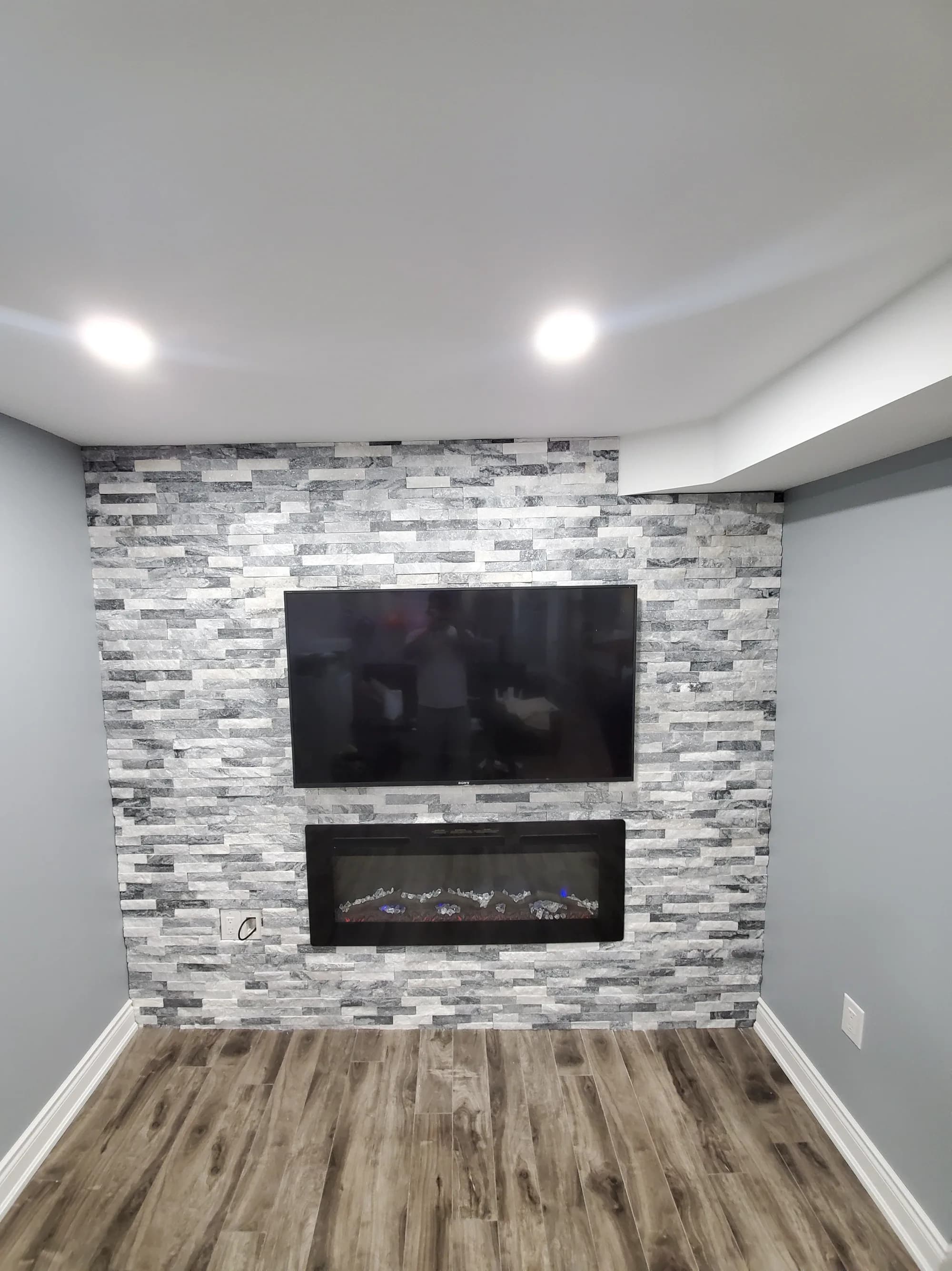 Basement media room with stone tile fireplace wall and built-in electric fireplace