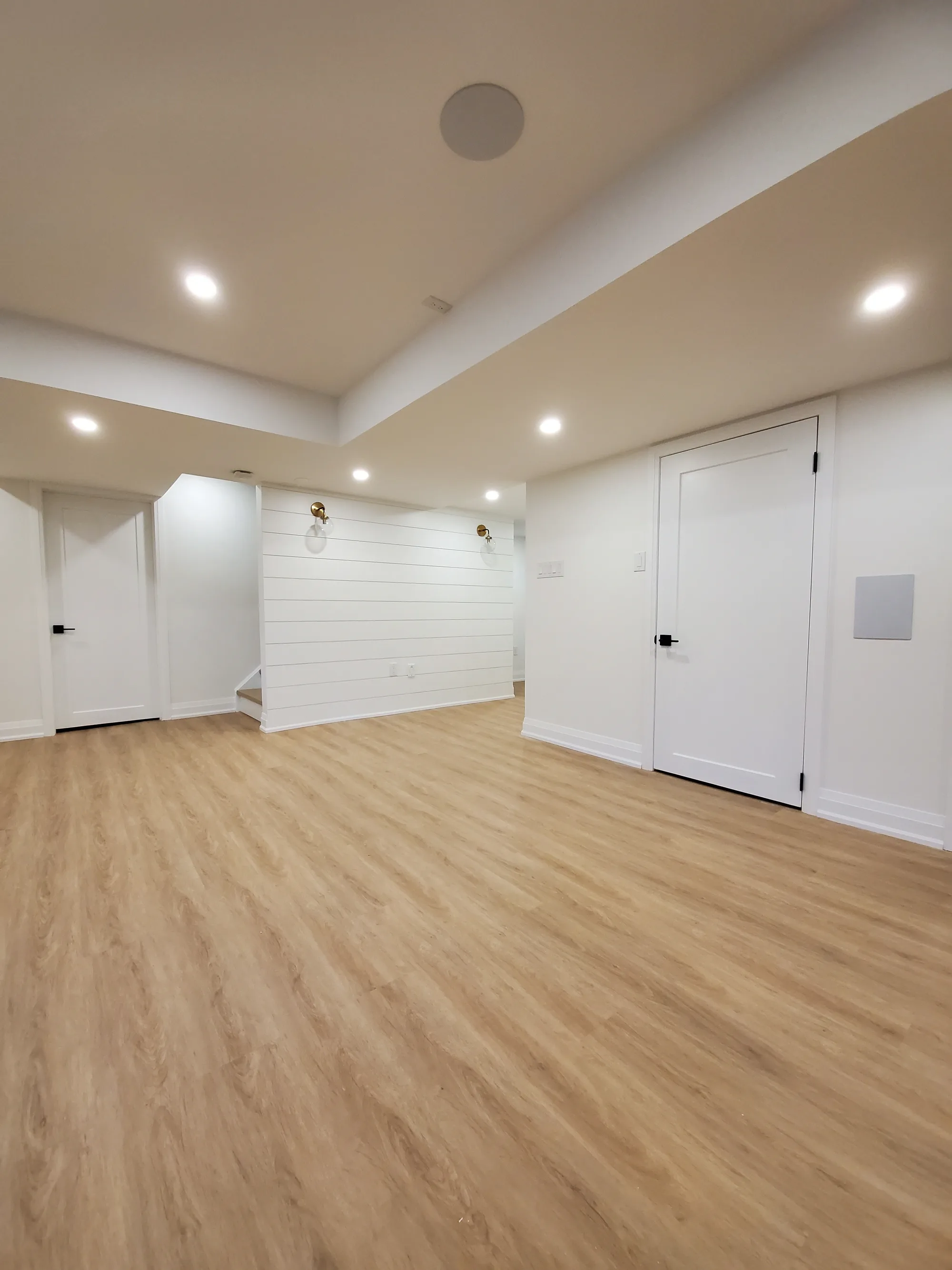 Bright basement living area with white shiplap accent wall and gold globe sconces
