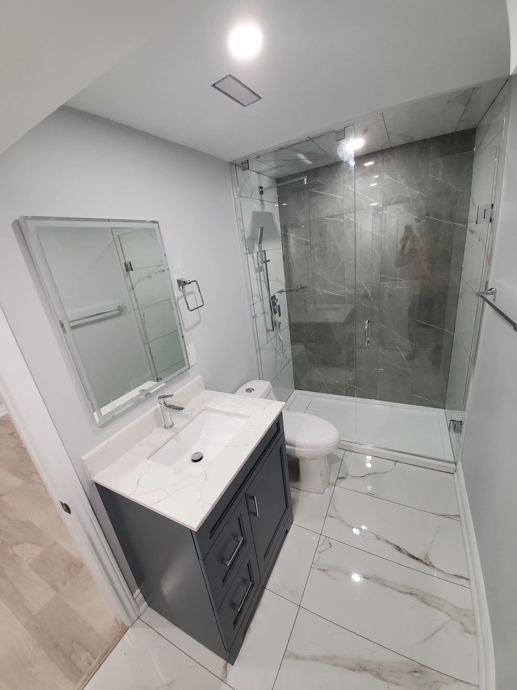 Basement bathroom with dark vanity, marble floor, and glass walk-in shower