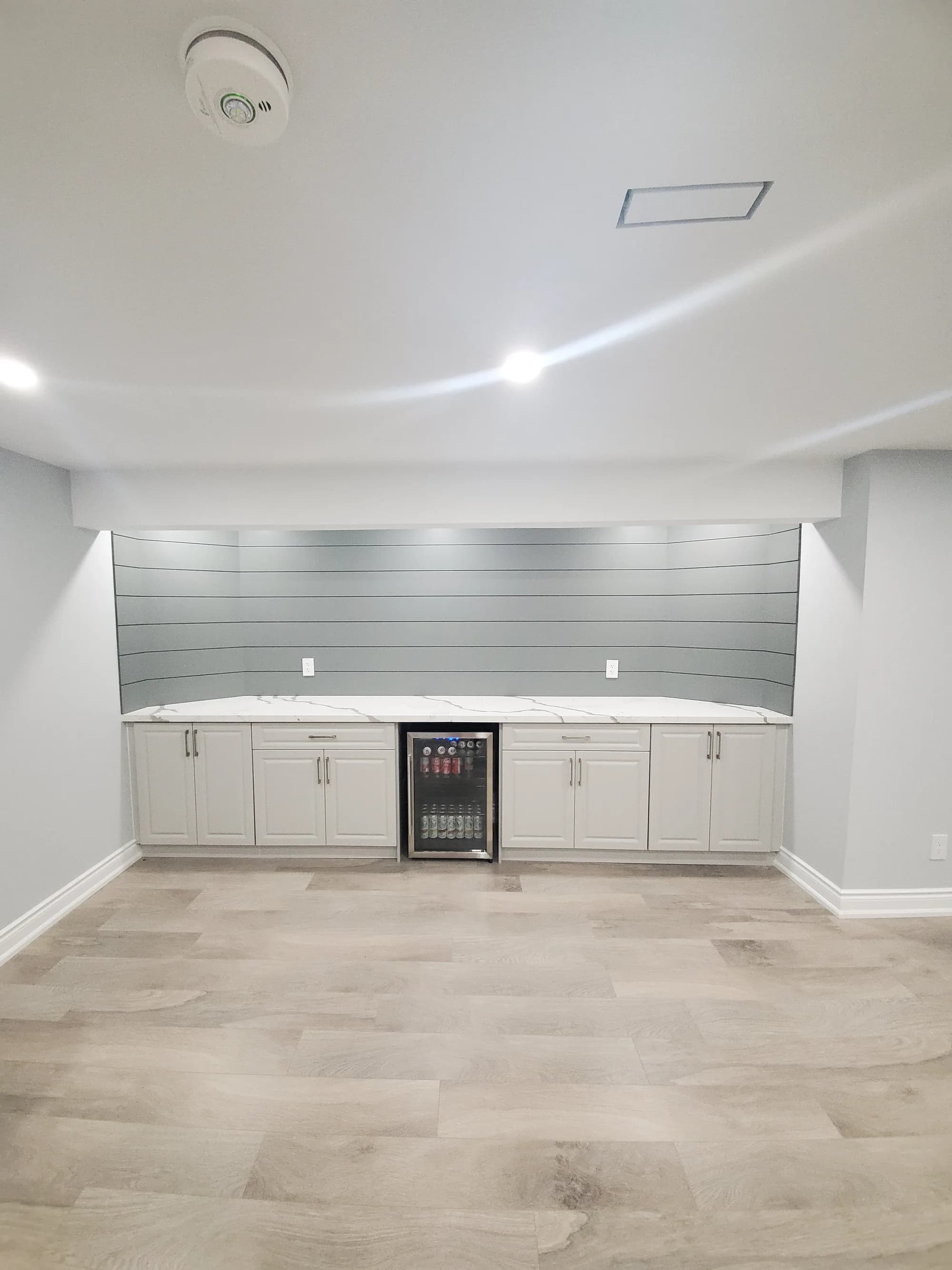 Basement bar area with white cabinets, quartz countertop, and beverage fridge