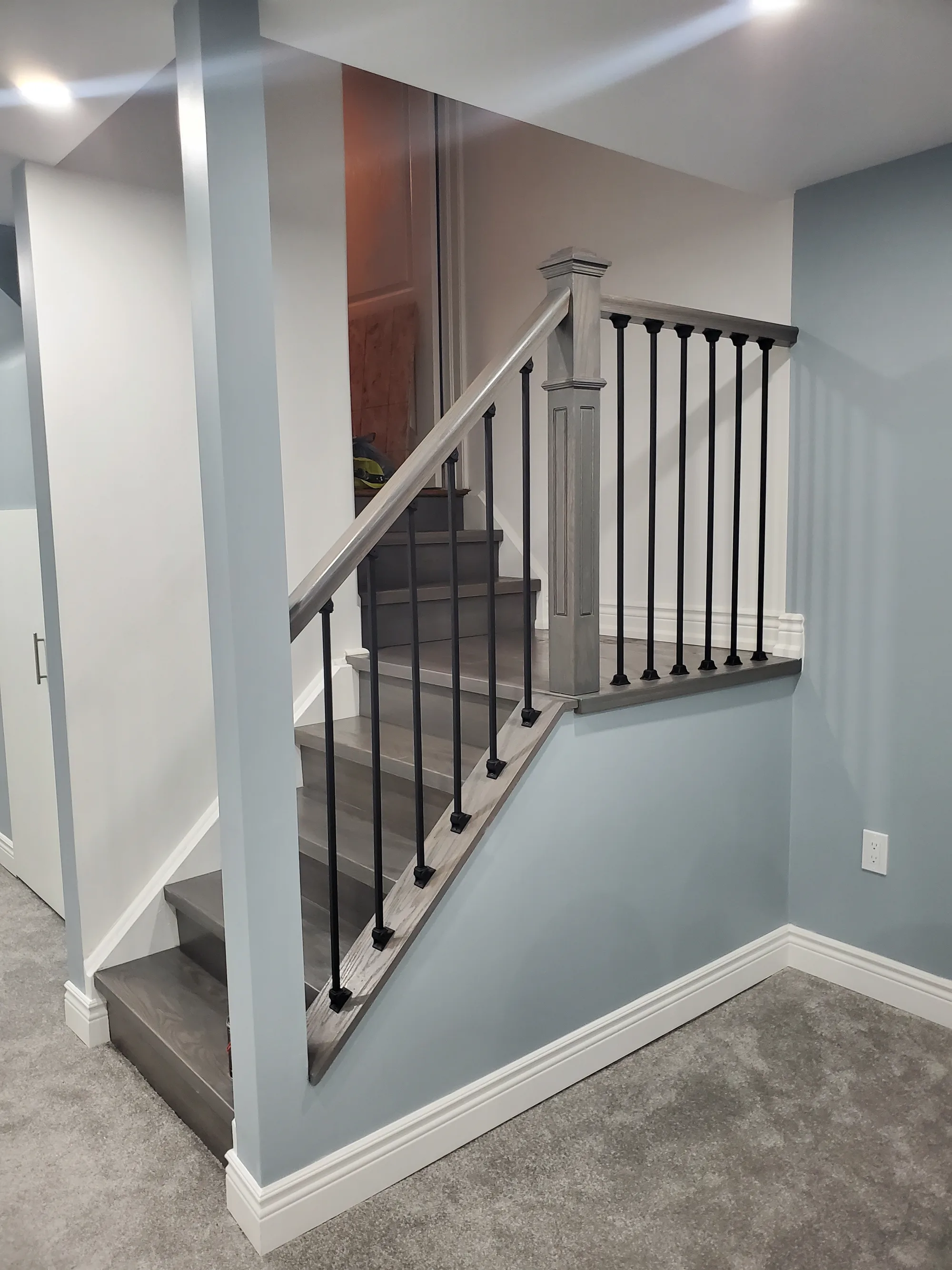 Basement staircase with grey wood treads and black iron spindles