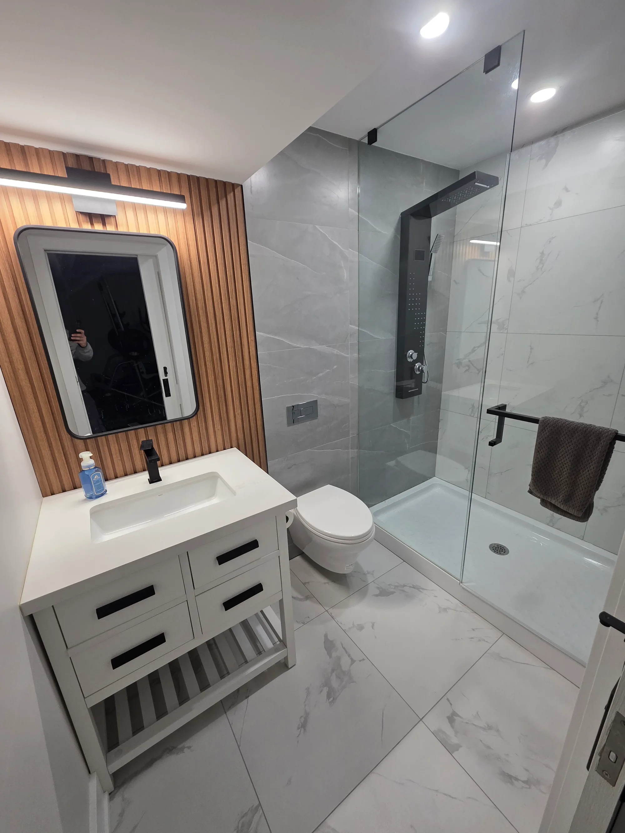 Basement bathroom with wood slat feature wall, walk-in glass shower, and marble tile