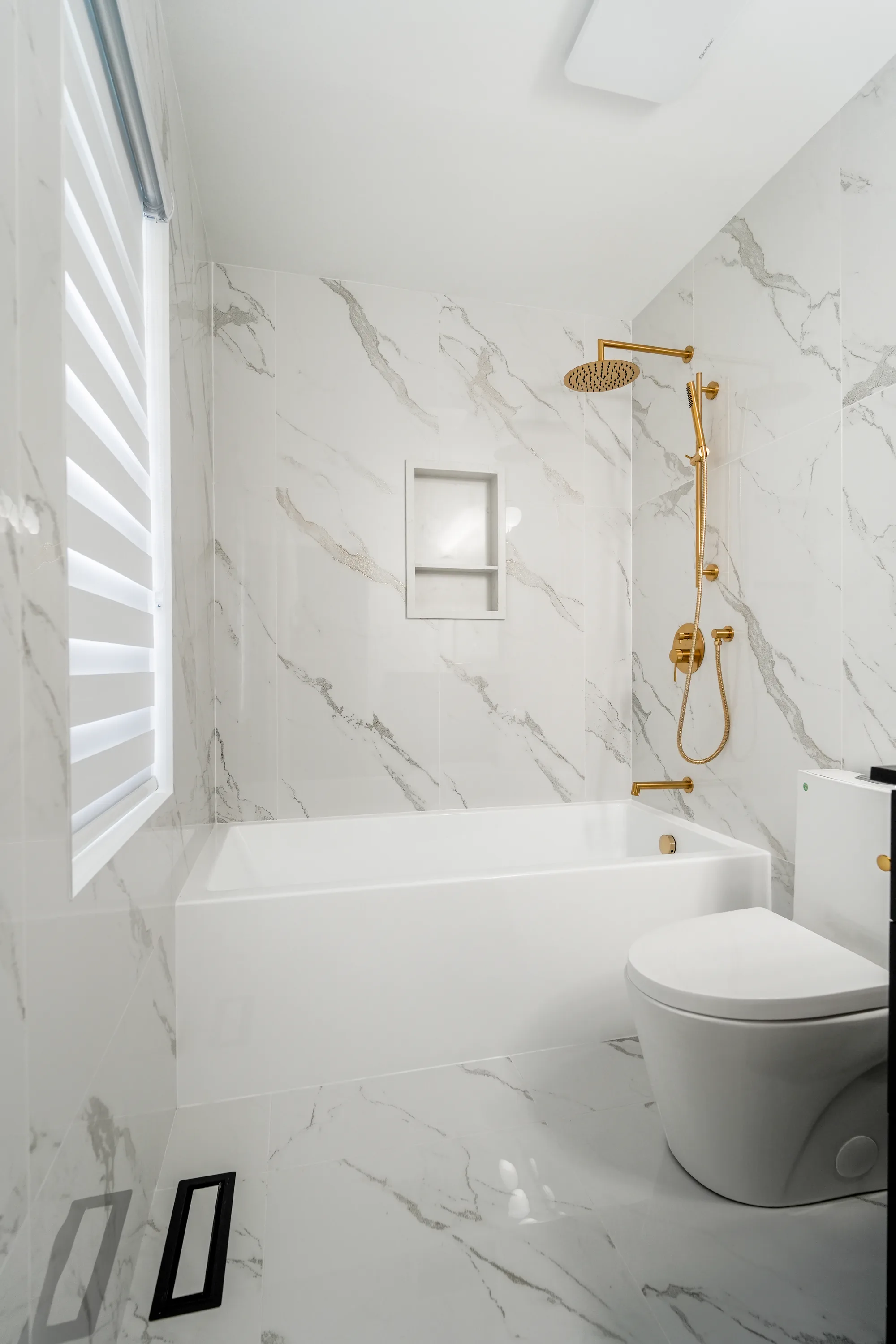 Marble bathroom with tub, toilet, and gold shower