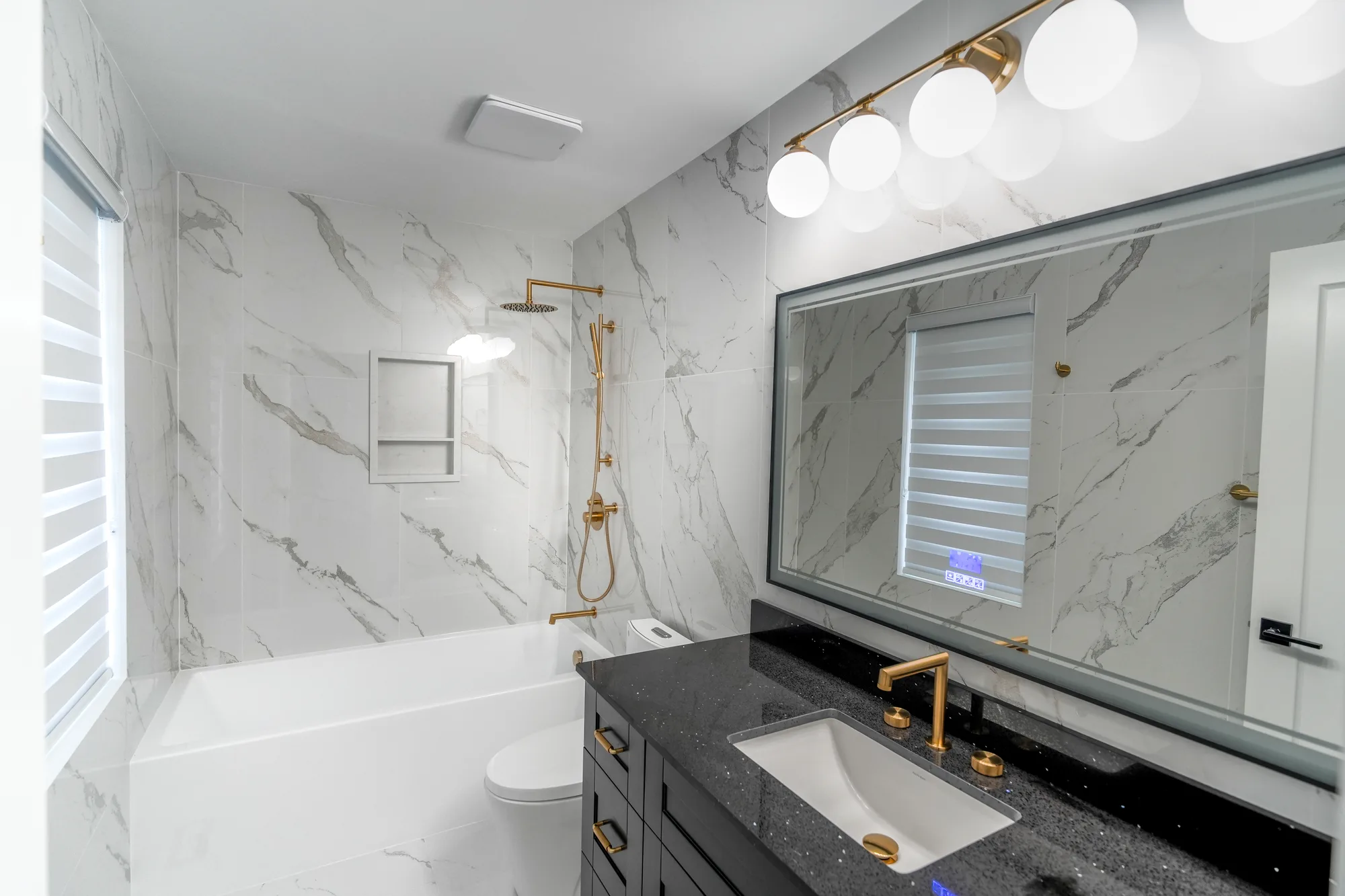 Master bathroom with marble tile, black vanity, and gold rain shower