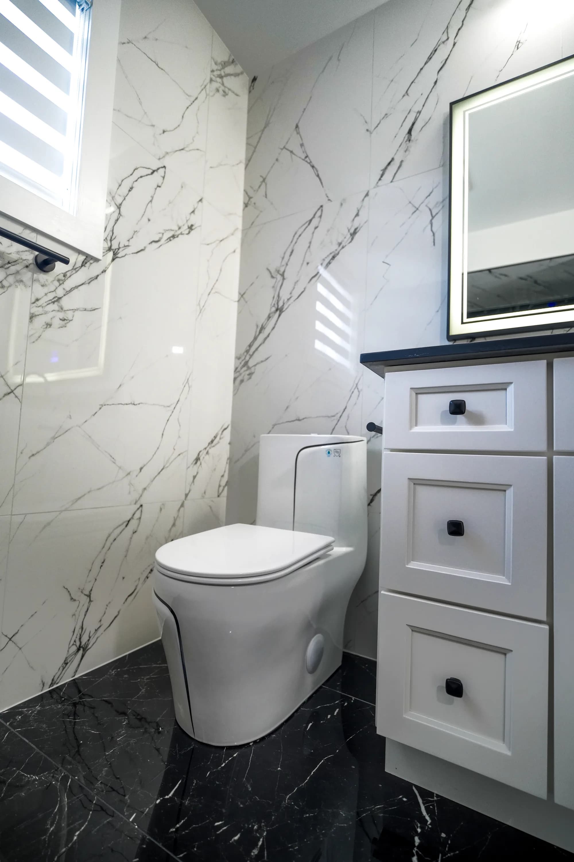 Compact powder room with marble walls and LED mirror