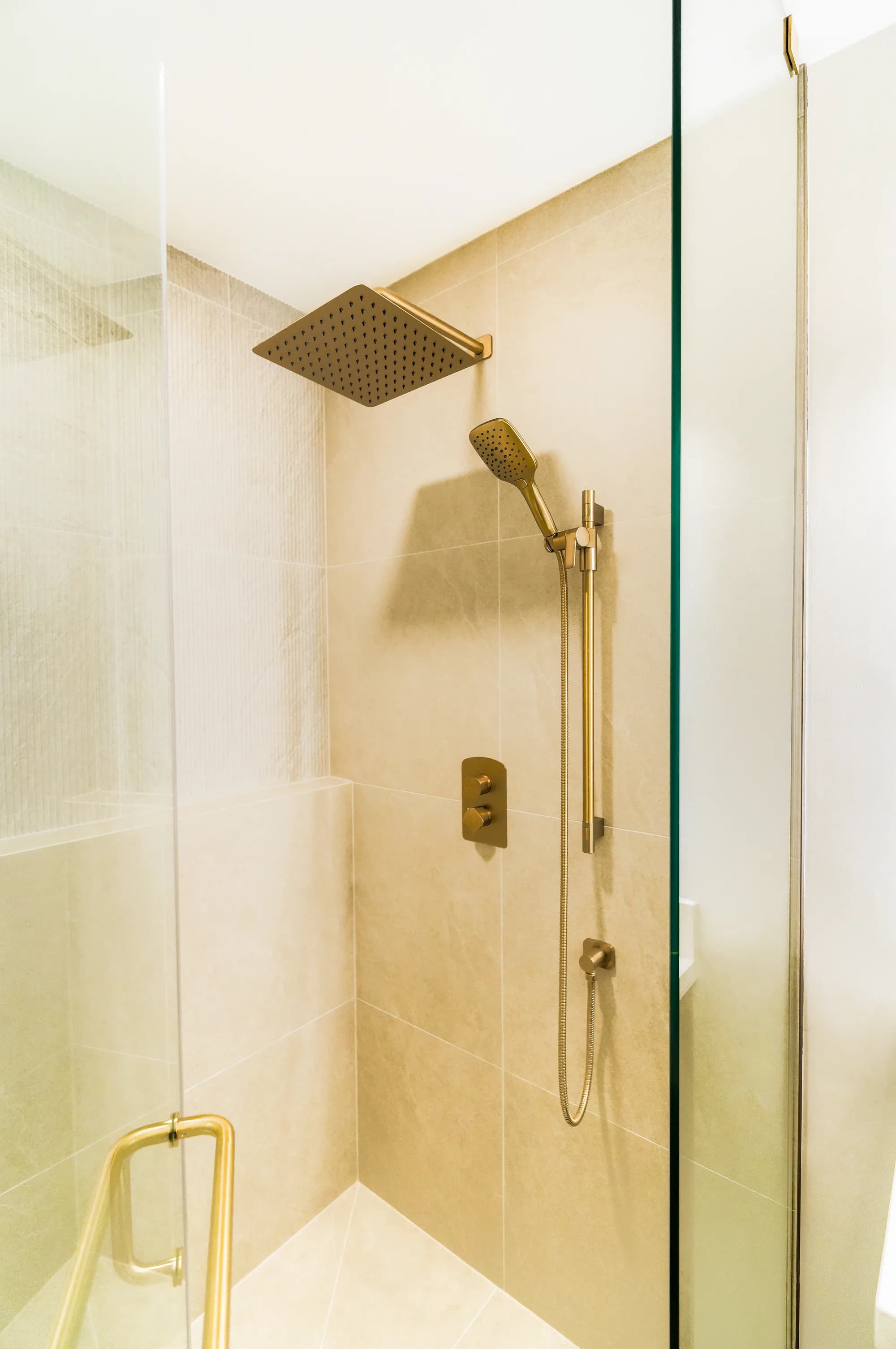 Walk-in shower with gold fixtures and neutral tile
