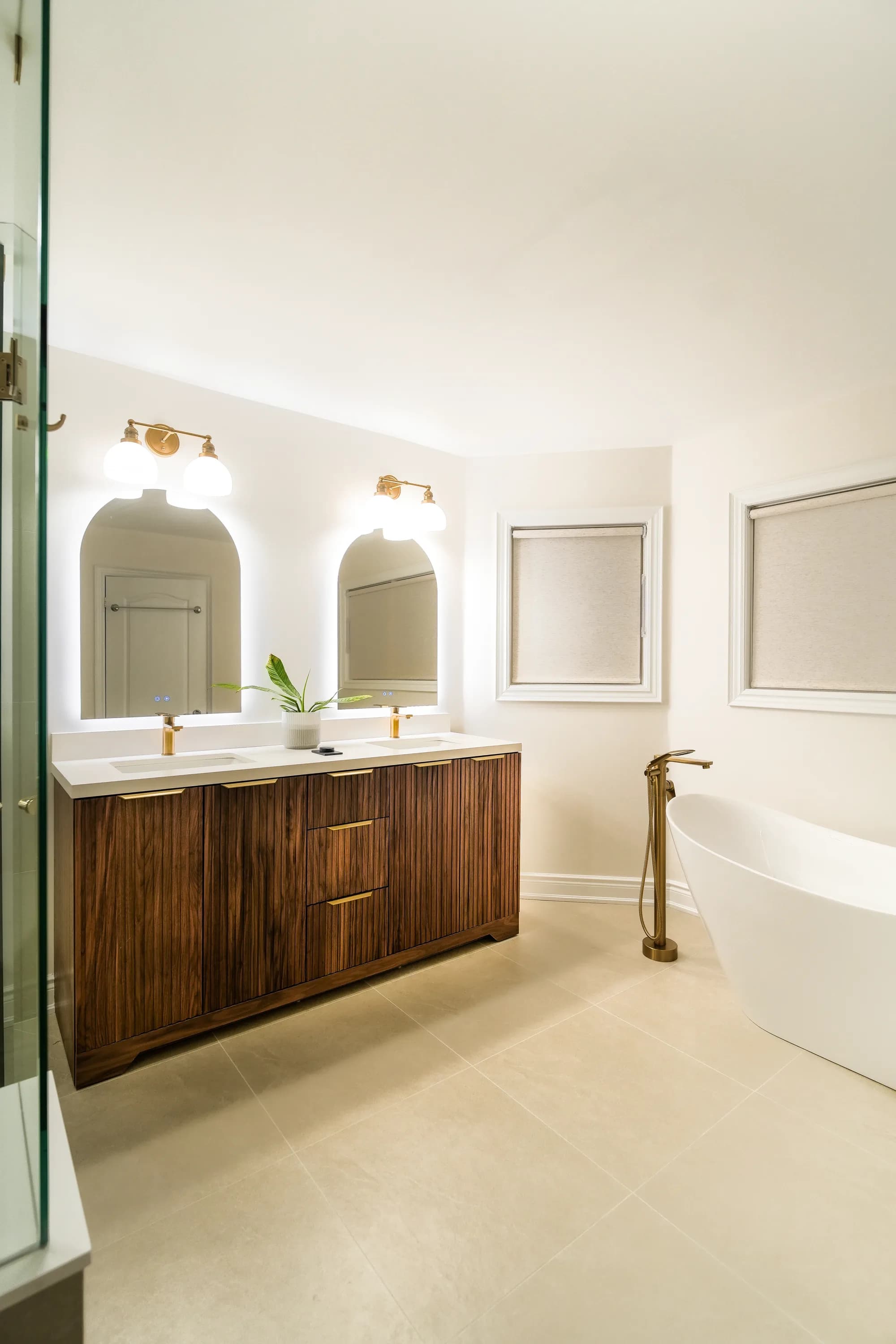 Luxury bathroom with walnut vanity, arched mirrors, and freestanding tub