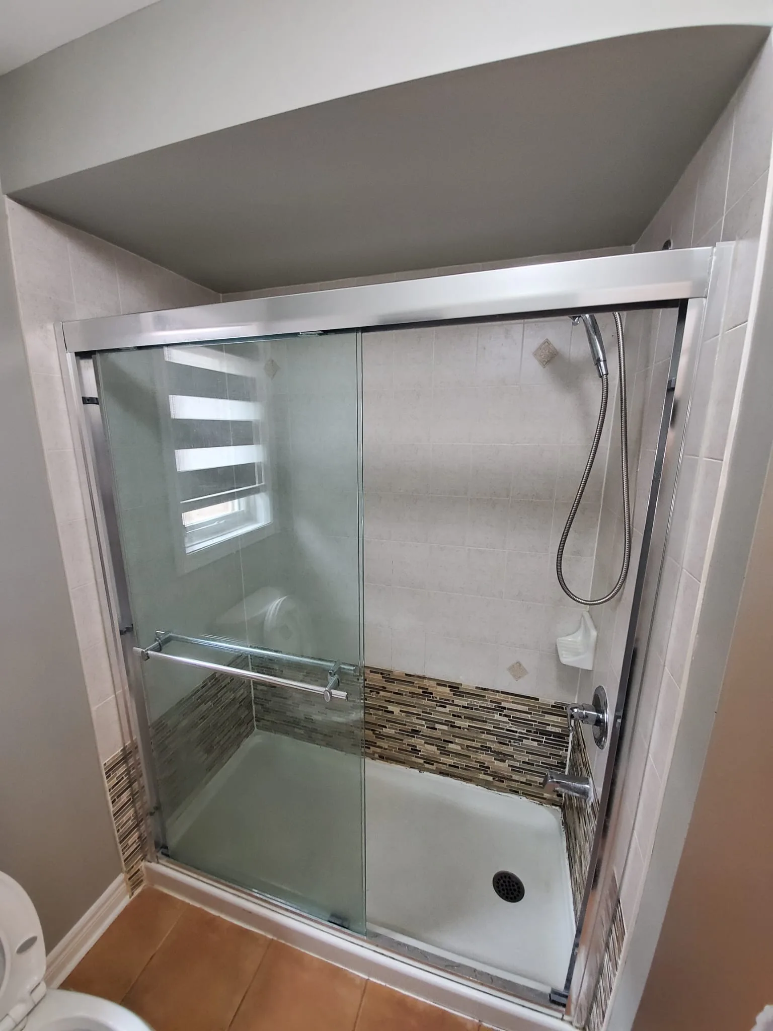Dated tub-shower combo with chrome sliding doors and worn mosaic accent tile