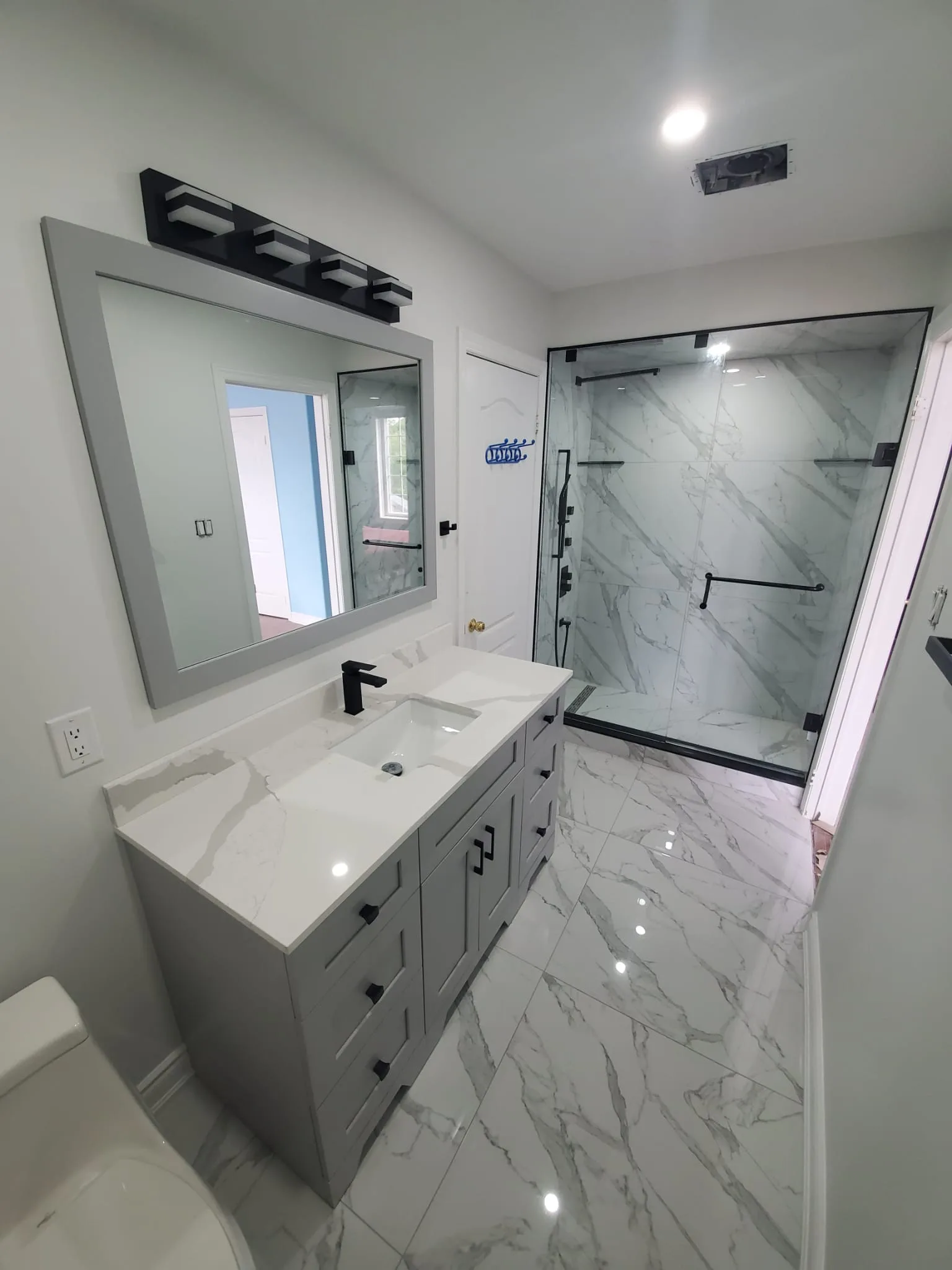 Modern bathroom with grey shaker vanity, quartz waterfall counter, frameless marble walk-in shower, and polished marble floor