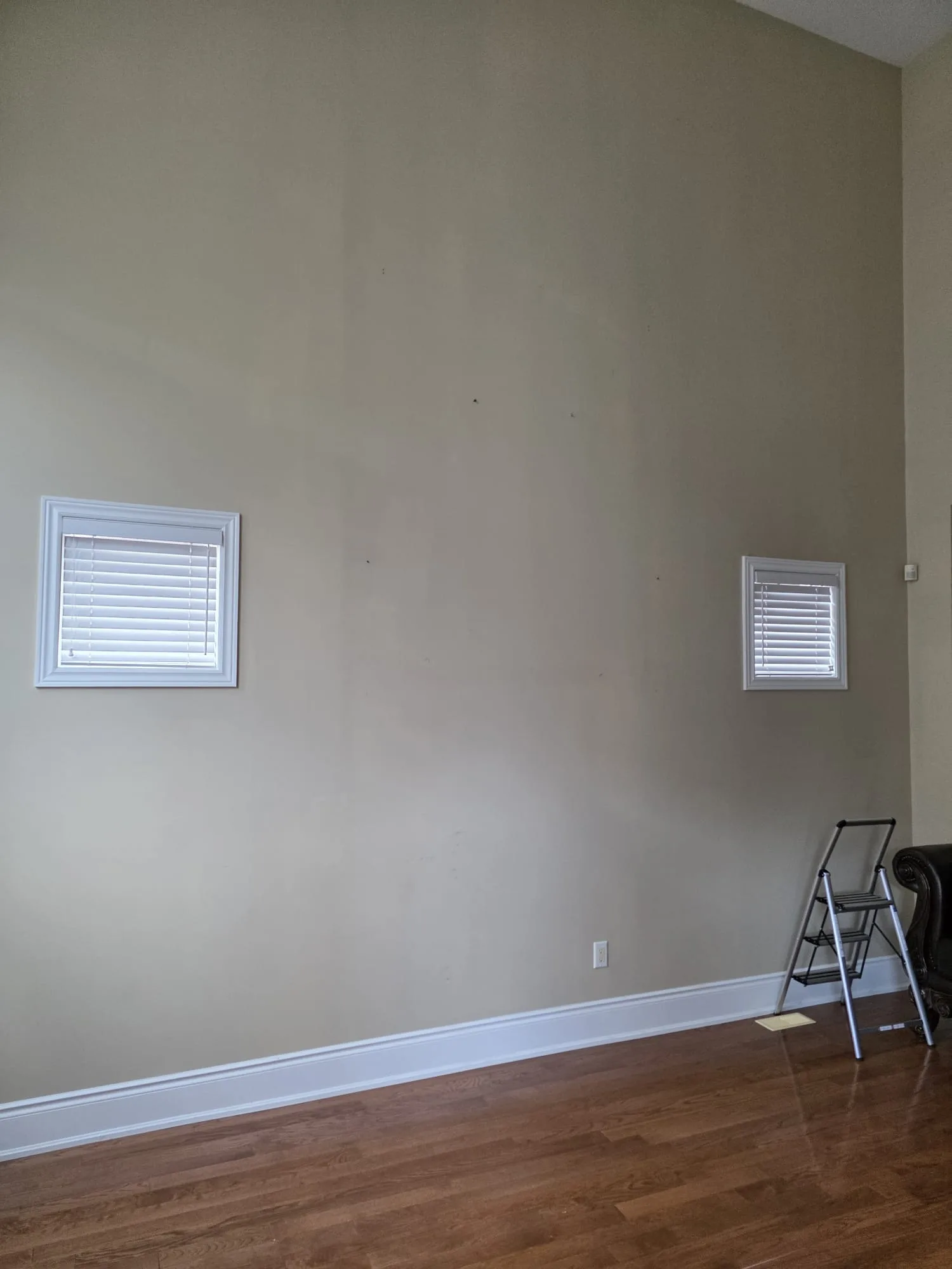 Empty taupe accent wall with two small recessed windows above hardwood floor